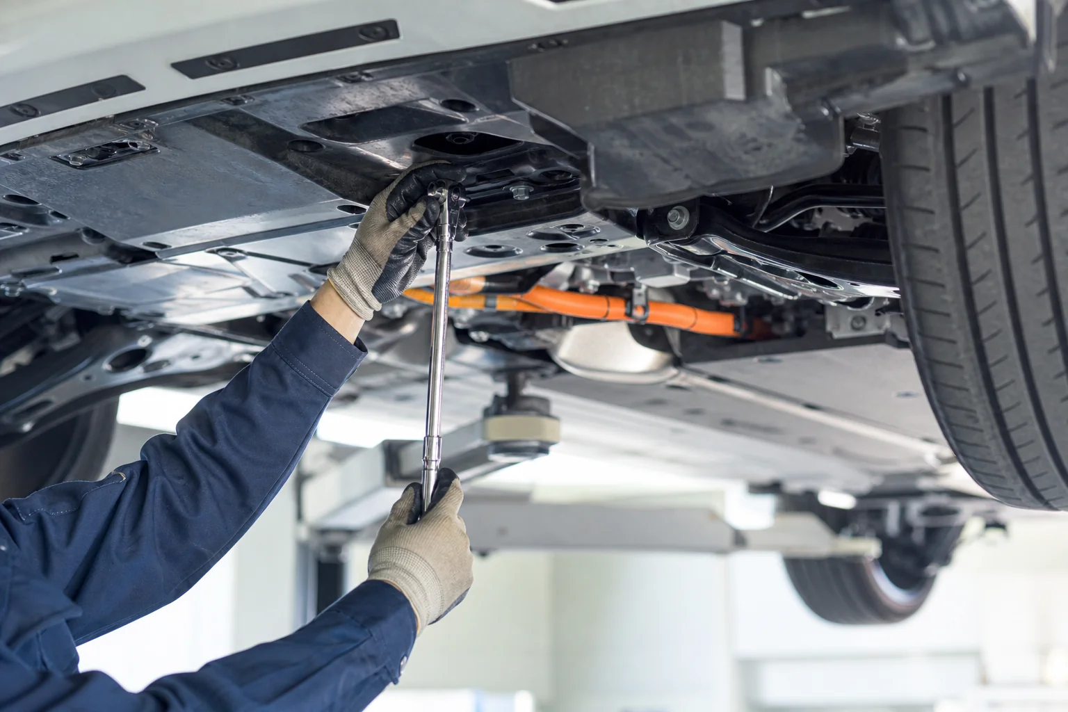 整備工場でハイブリッド車の下回りを点検する整備士の手元